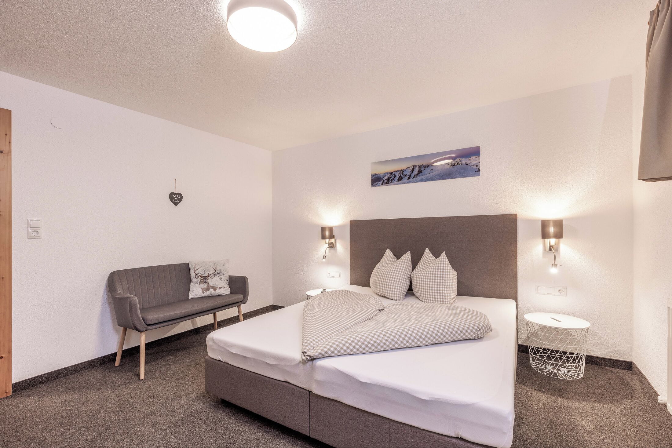Una habitación de hotel moderna con una cama, un sofá y dos lámparas fijadas a la pared.