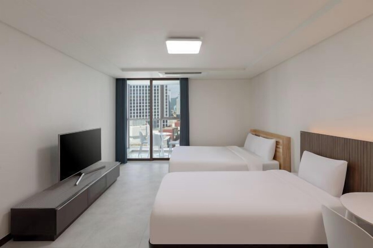 A hotel room with a flat-screen TV, two beds, a sofa, and a sliding glass door leading to an outdoor area.