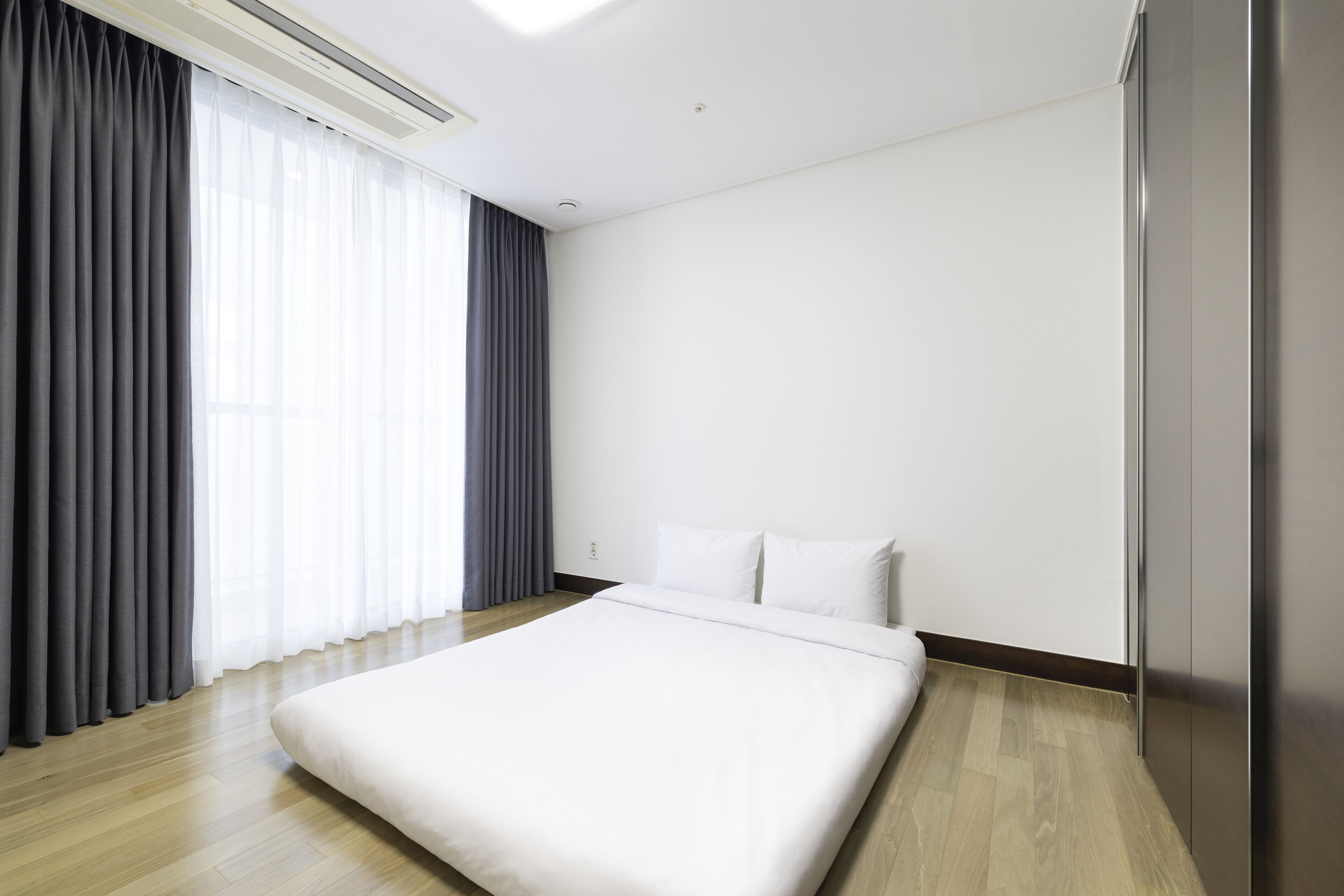 Une chambre d’hôtel moderne avec un grand lit, un plancher en bois et une grande fenêtre avec des rideaux.