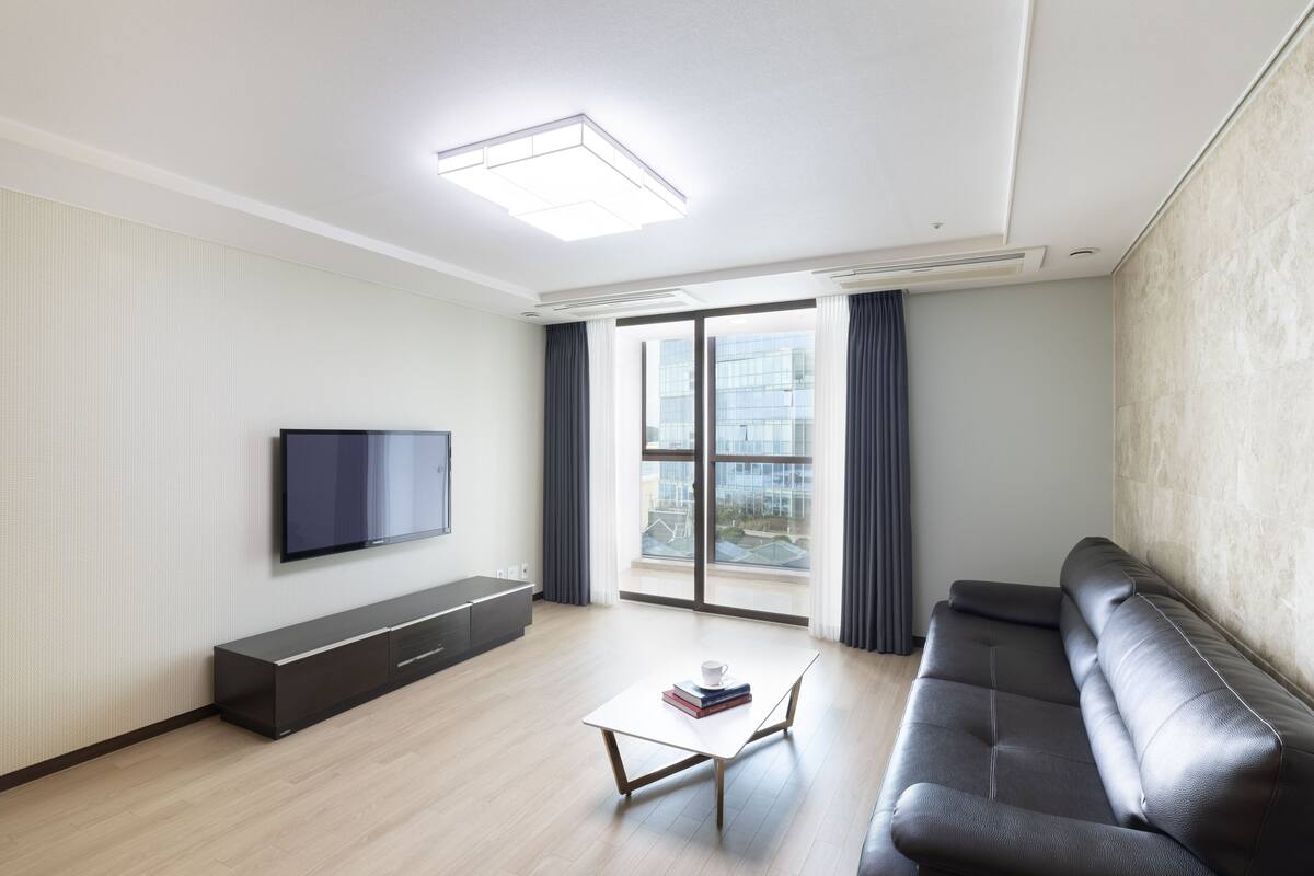 Una sala moderna con televisor de pantalla plana, un sofá, una mesa de centro y una puerta corrediza de vidrio a un balcón.