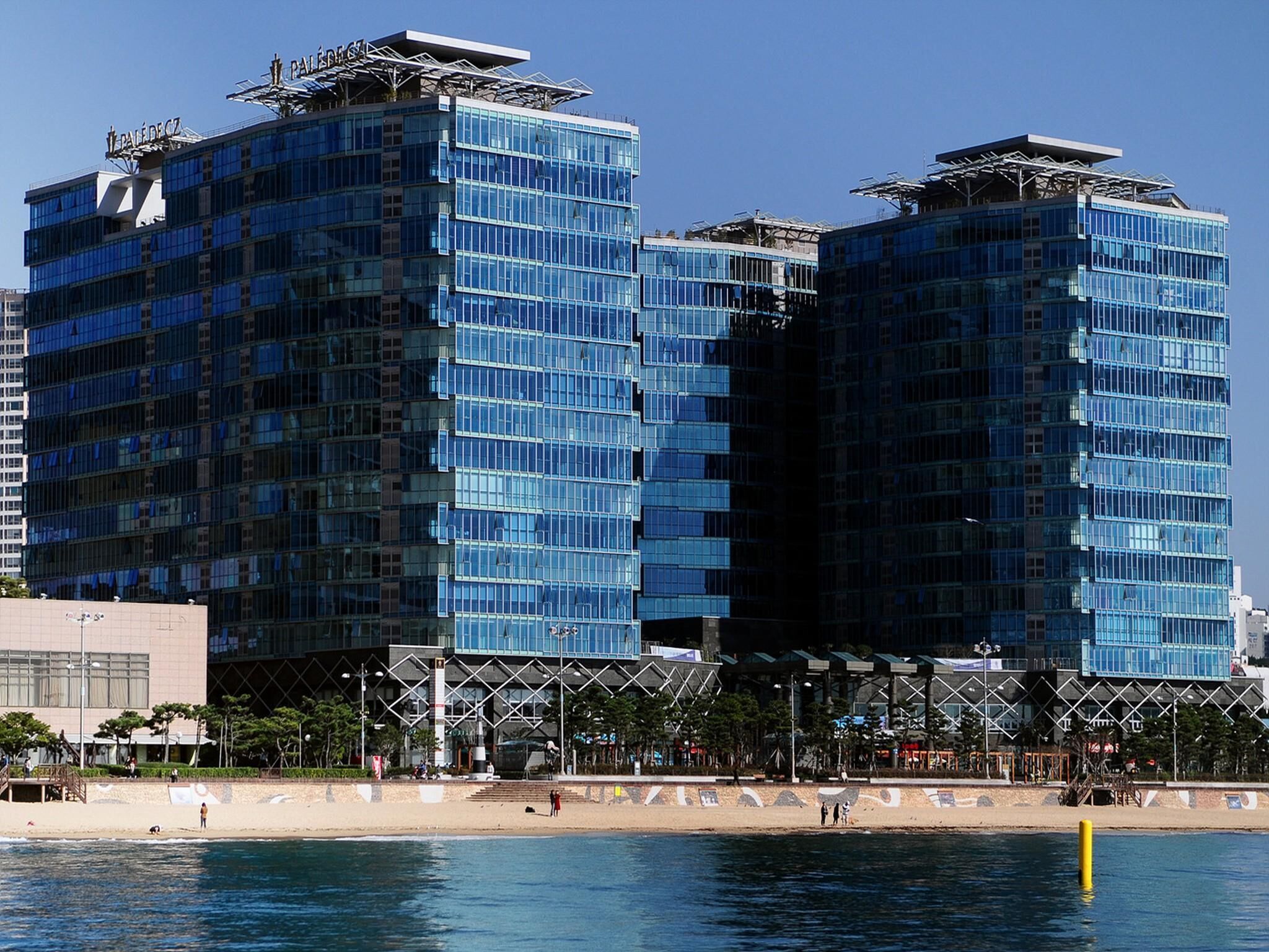 A modern building with a glass facade, located near a waterfront.