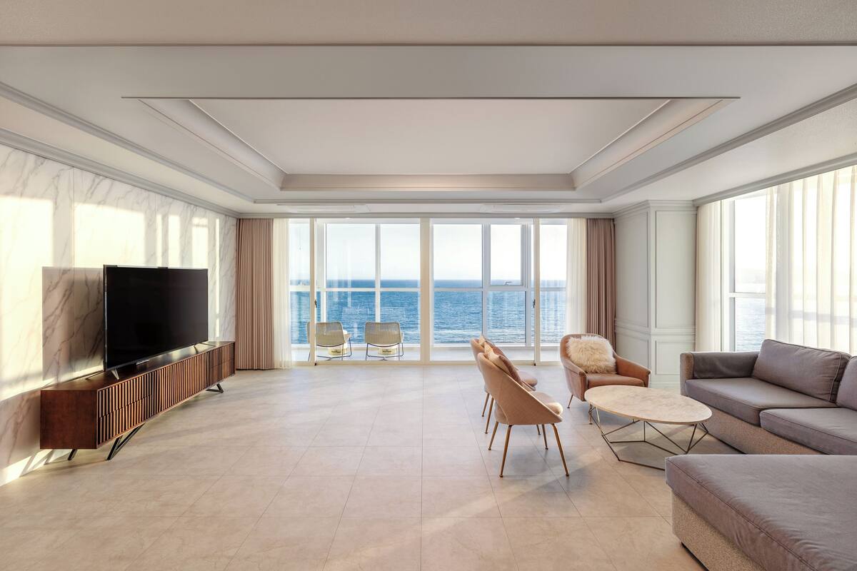 Un salón amplio con televisor grande, asientos cómodos y vista al mar.