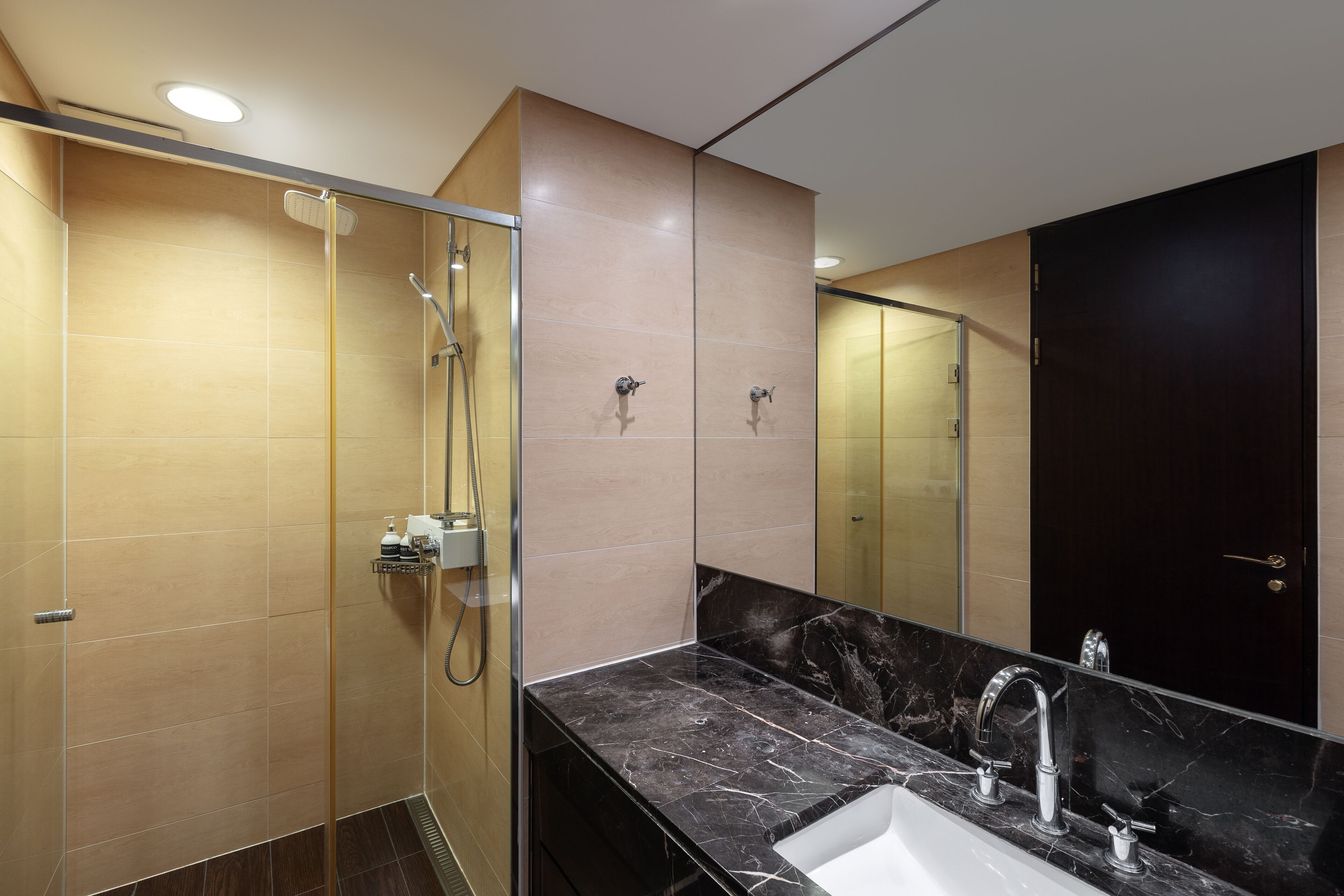 Un baño moderno con ducha envuelta en vidrio, lavabo de mármol y un espejo grande.