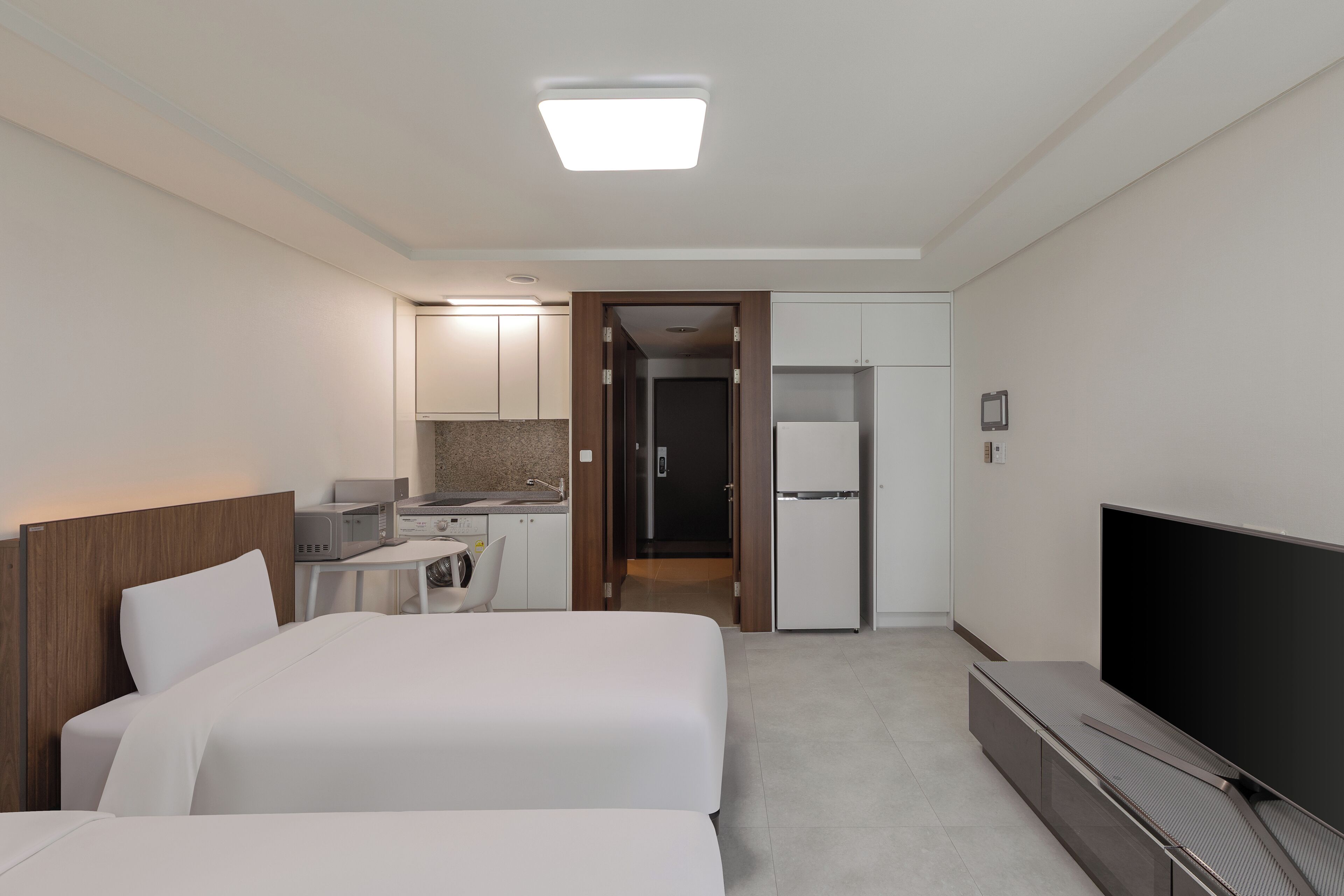 Quarto de hotel com duas camas, televisão, escrivaninha com computador, frigorífico e micro-ondas.