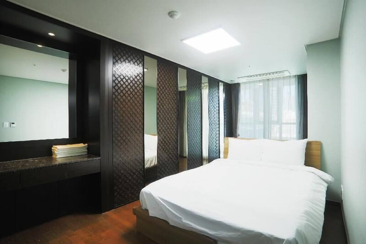 Una habitación de hotel moderna con una cama grande, un escritorio integrado y un espejo amplio.