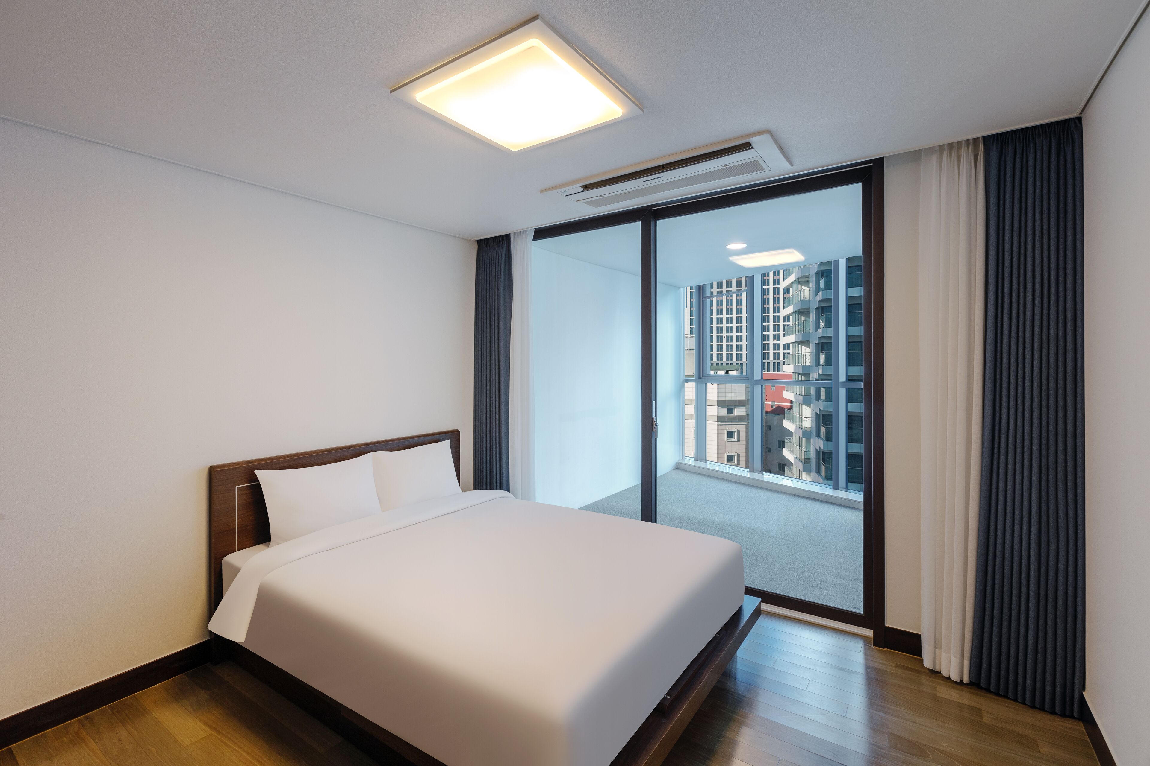A hotel room with a large bed, a window with curtains, and a view of buildings.