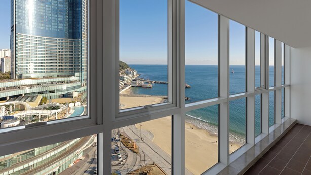 A high-rise hotel room with large windows overlooking a beach and a cityscape. - Pale De CZ (Busan)
