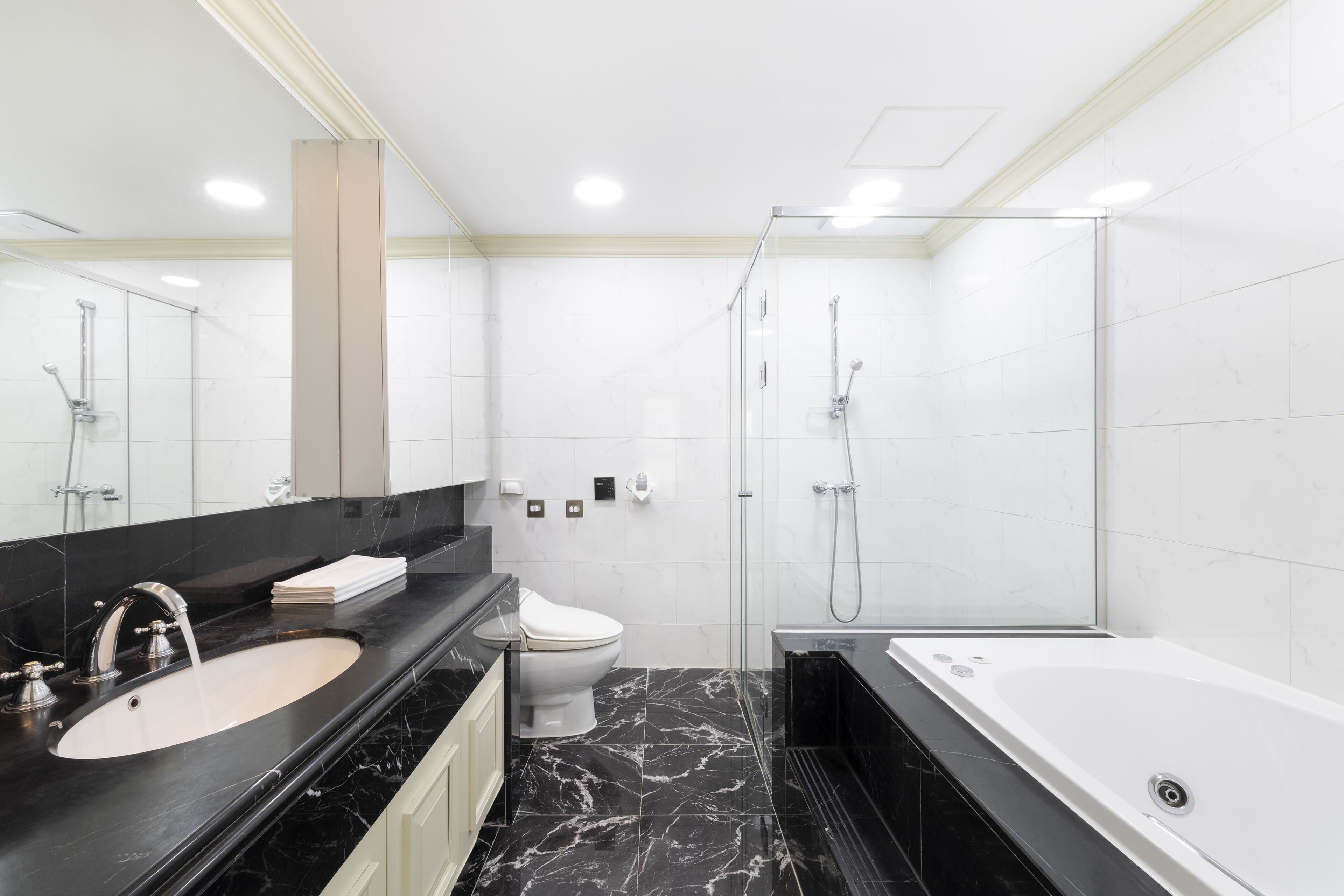 Une salle de bain moderne avec un lavabo en marbre noir, des toilettes blanches, une douche en verre et une baignoire blanche.