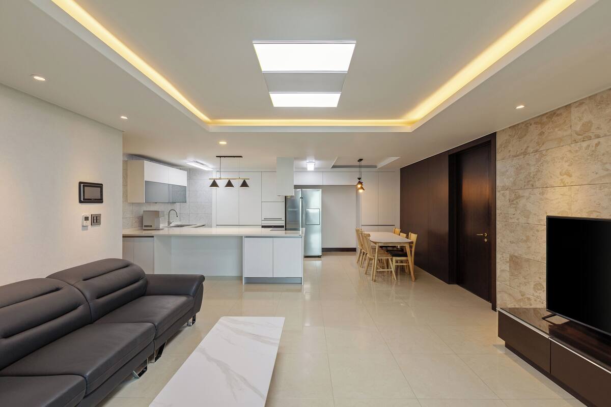 Una sala de estar moderna con un sofá, un comedor con sillas, un televisor y una cocina con armarios y electrodomésticos.