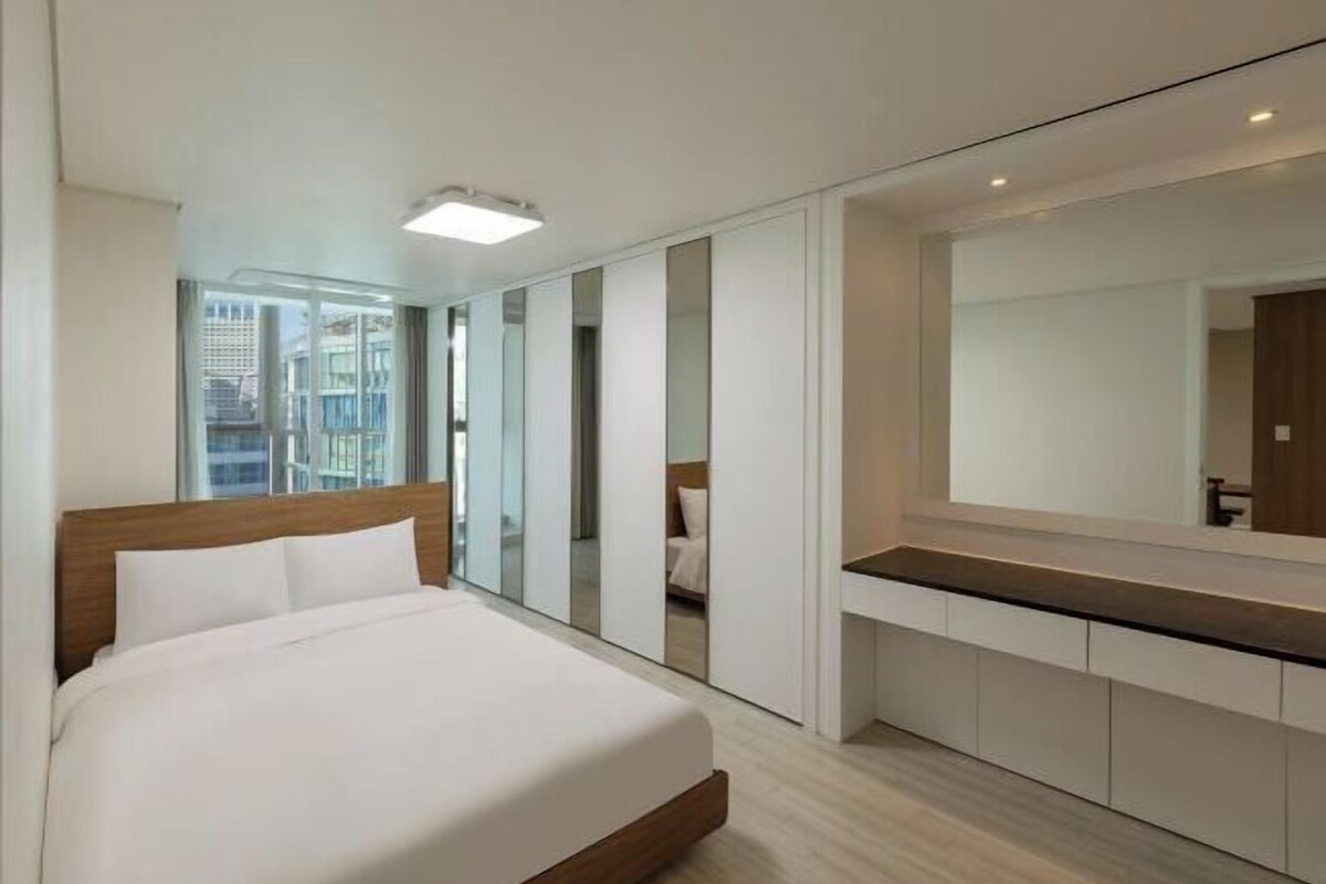 A modern hotel room with a large bed, a built-in desk, a large mirror, and a city view.