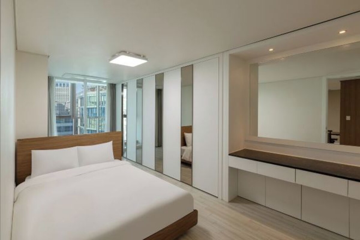 Ett modernt hotellrum med en stor säng, ett inbyggt skrivbord, en stor spegel och utsikt över staden.