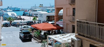 A marina with boats, a ticket office, parked cars, and potted plants.