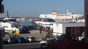 Um movimentado porto com várias embarcações atracadas, uma ponte para pedestres e carros estacionados ao longo da costa.