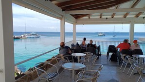 Uma área de estar coberta ao ar livre, com mesas e cadeiras, com vista para uma marina com barcos.