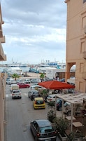 A marina with boats docked, a parking area with cars, and a building with balconies.