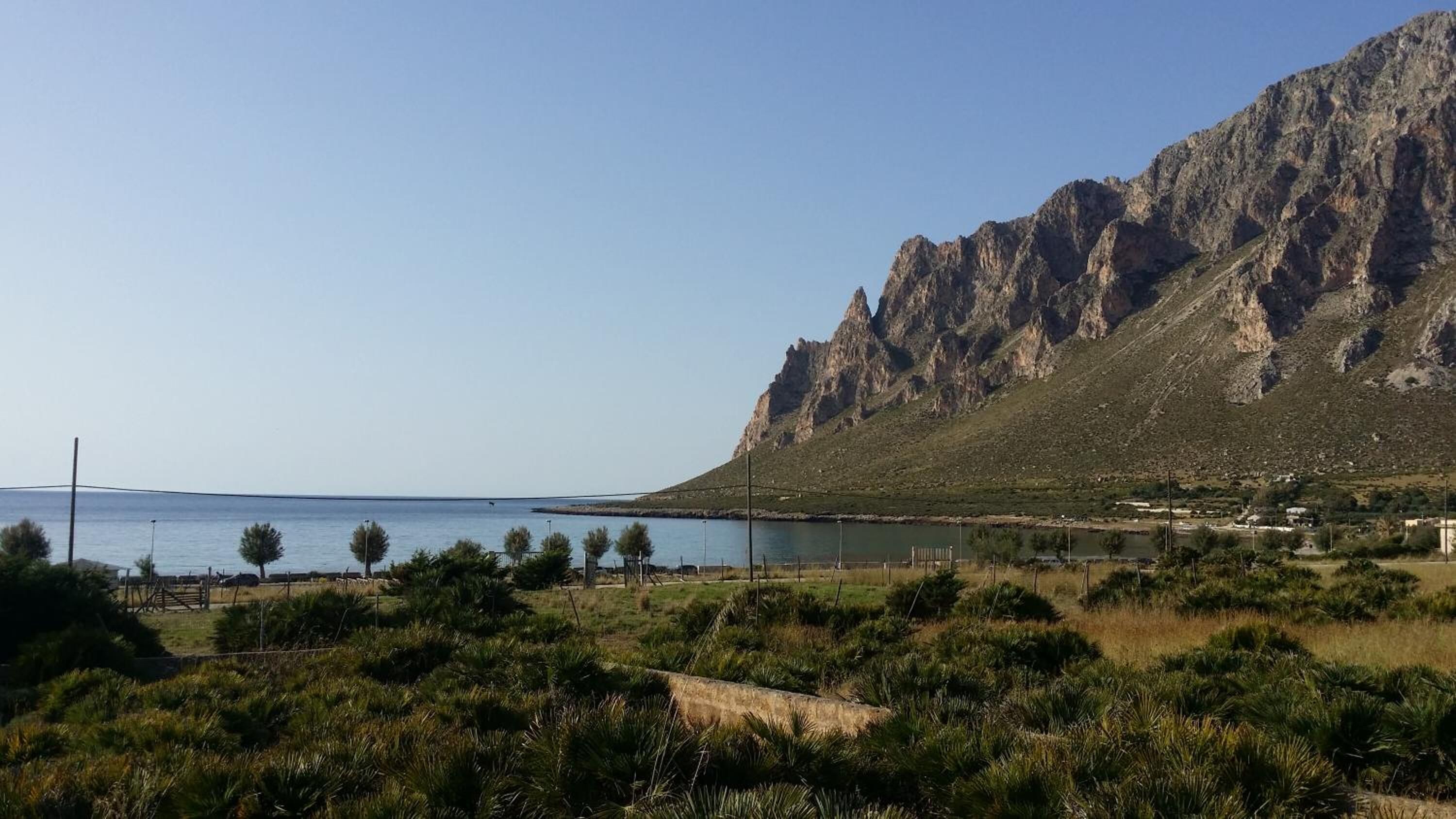 A coastal landscape with a rocky mountain, a body of water, and sparse vegetation.