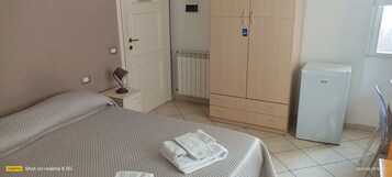 Una camera da letto con un letto, un comodino, una lampada, un armadio, un termosifone e un piccolo frigorifero.