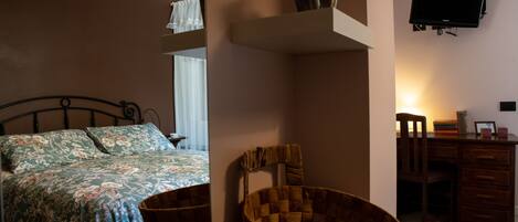 A bedroom with a bed, a wicker chair, a desk, and a television mounted on the wall.
