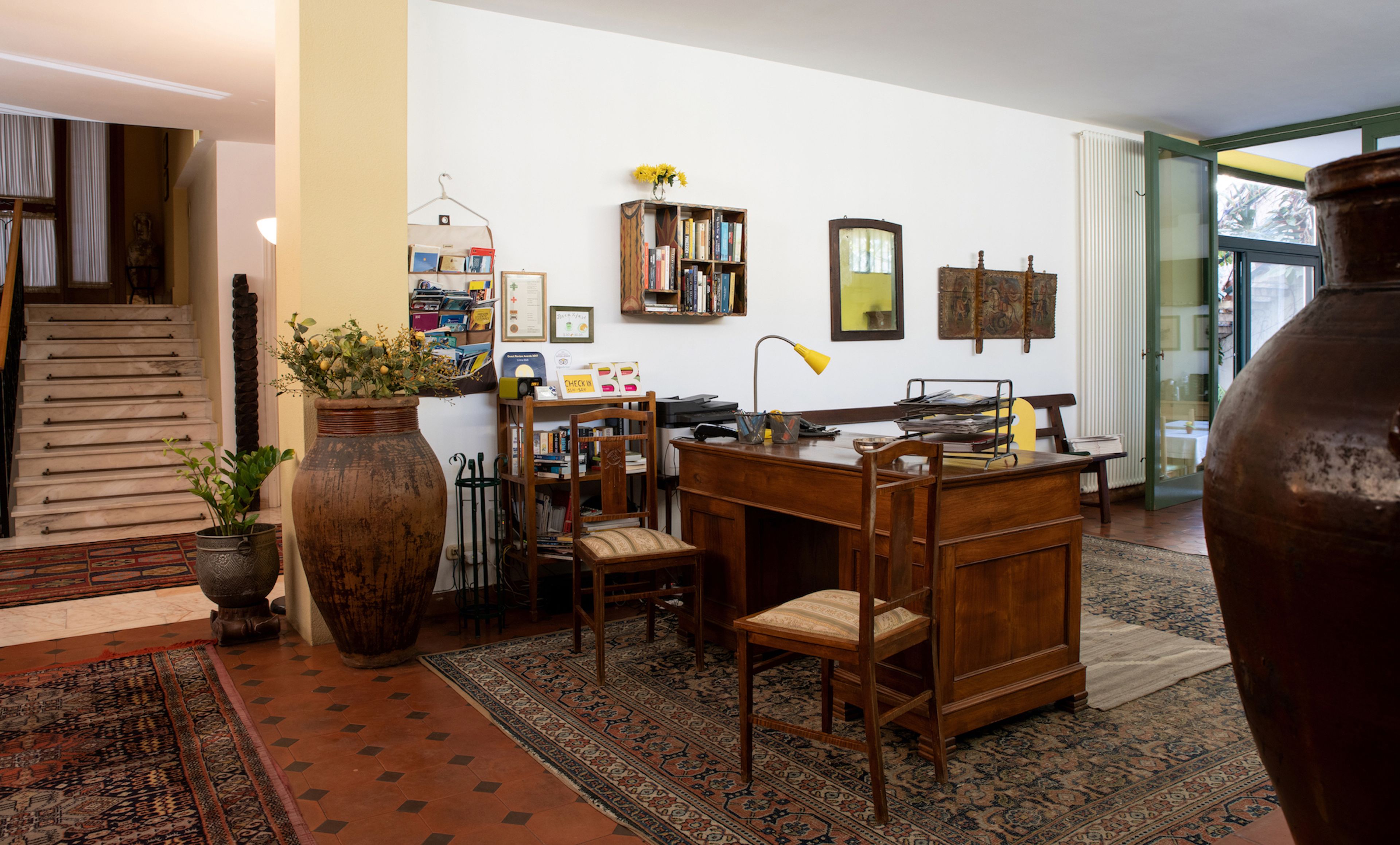 A spacious living room with a large wooden desk, a bookshelf, and a large vase with flowers.
