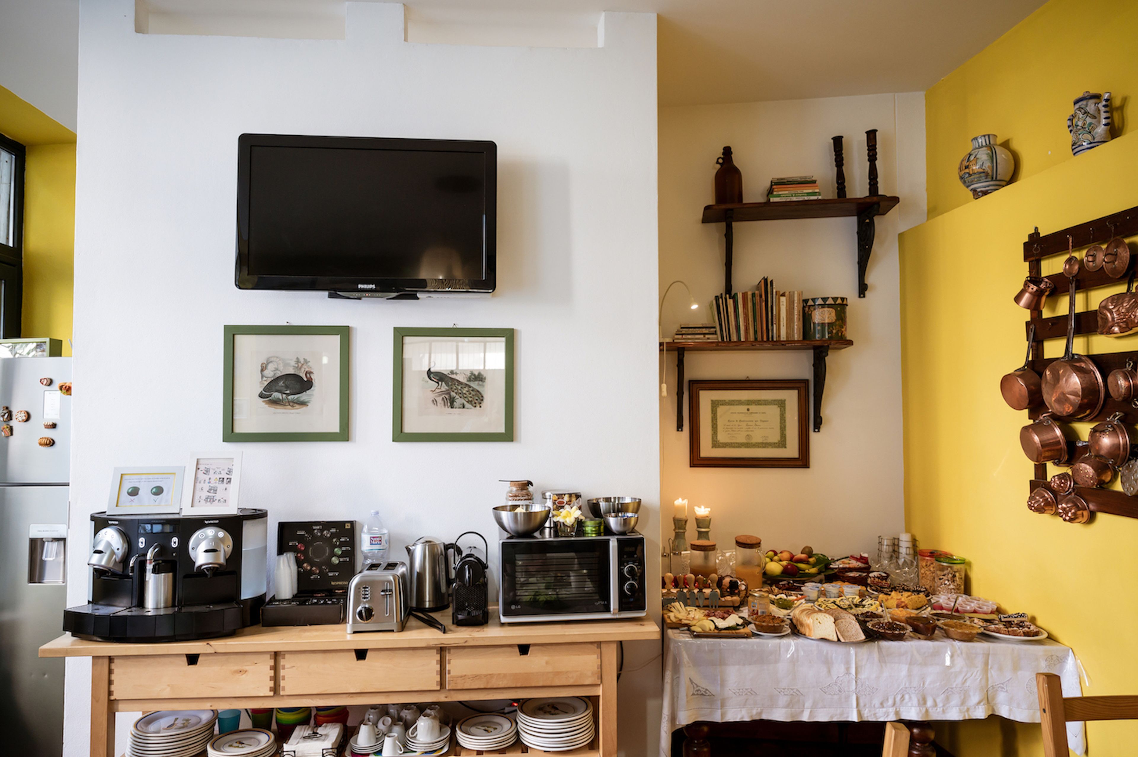 A kitchen with a TV, coffee machines, a microwave, and a dining table set with food.