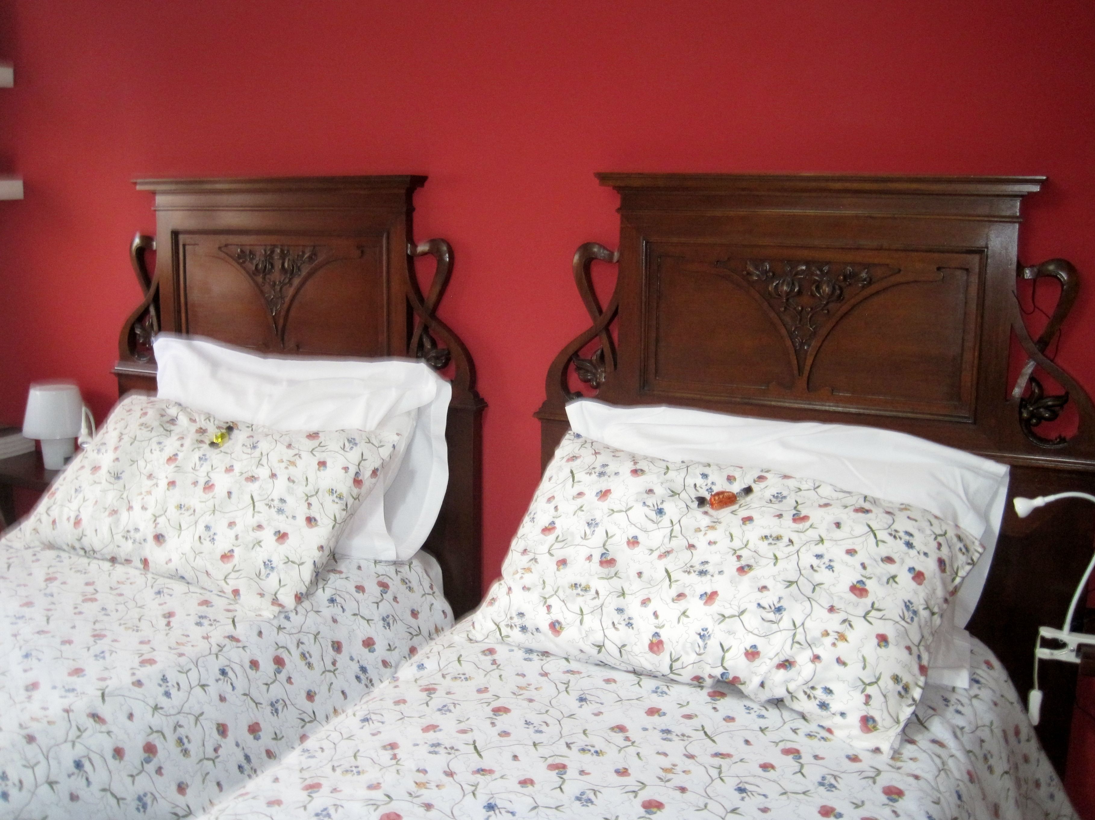 Dos camas de madera con ropa de cama floral frente a una pared roja.