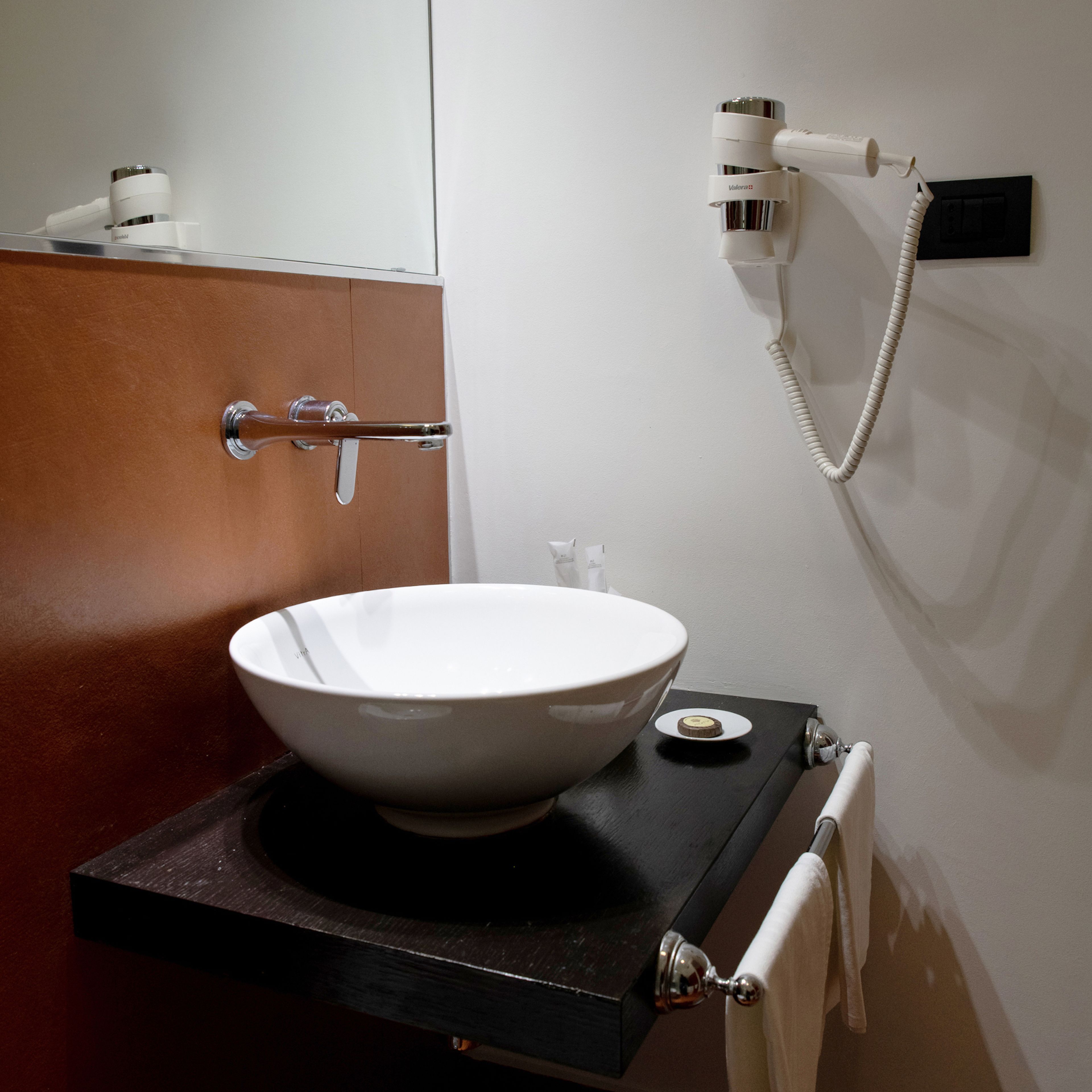 A bathroom with a white sink on a black countertop, a towel rack, and a hairdryer mounted on the wall.