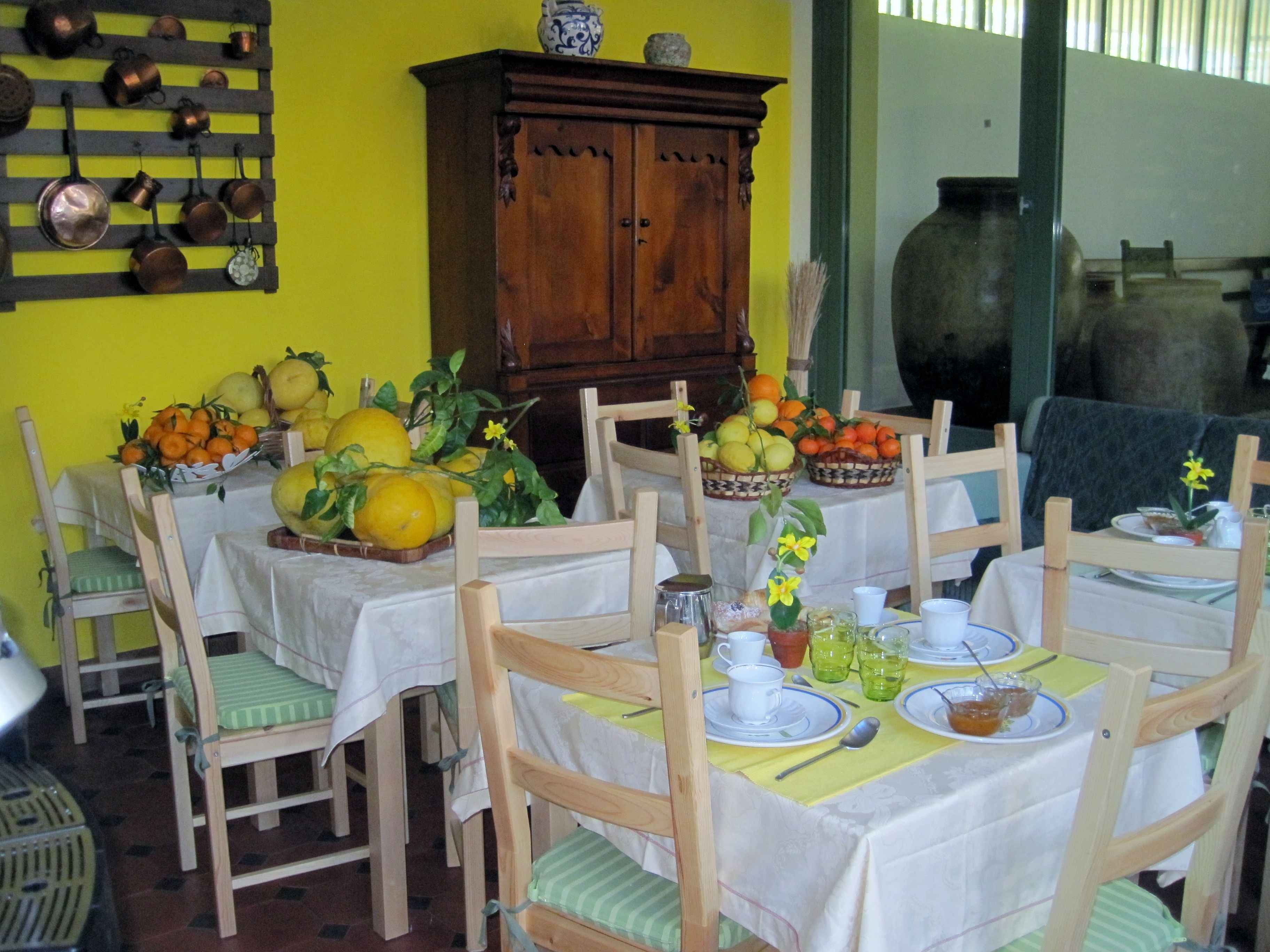 Un coin repas avec une table dressée pour quatre personnes, entourée de chaises en bois avec des coussins verts. On aperçoit, au fond, un buffet en bois orné d’objets décoratifs.