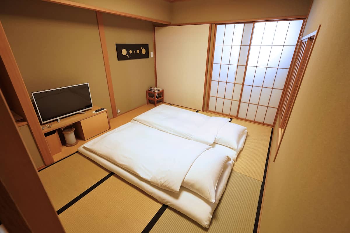 A traditional Japanese room with tatami flooring, a futon bed, a television, and a sliding shoji screen.