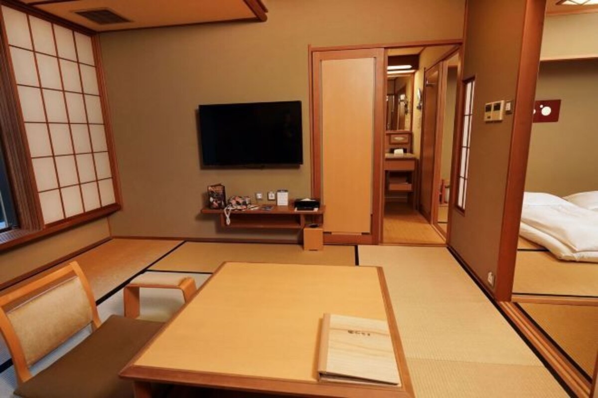 A traditional Japanese-style room with tatami flooring, a low table, a chair, a television, and a sliding door leading to another room.
