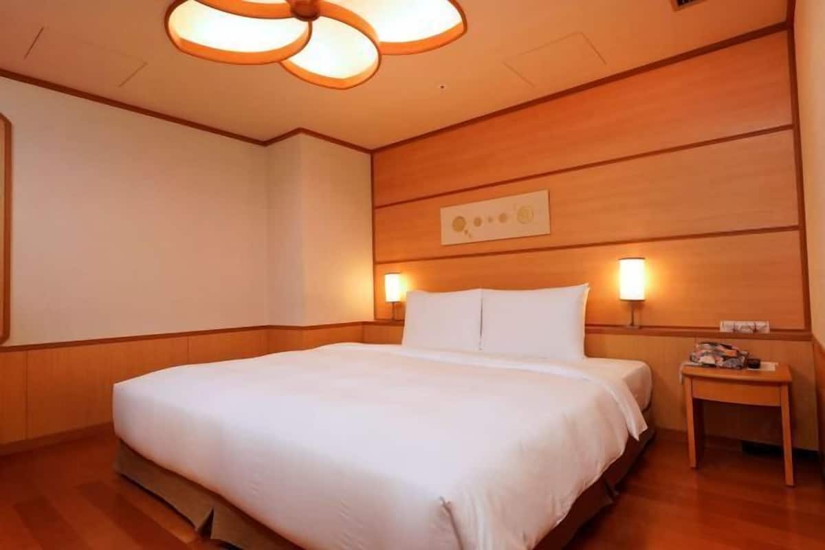 A hotel room with a large bed, wooden paneling, two bedside lamps, and a ceiling fan.