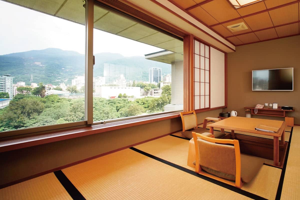 A traditional Japanese room with tatami flooring, a low table, and a view of a cityscape through large windows.