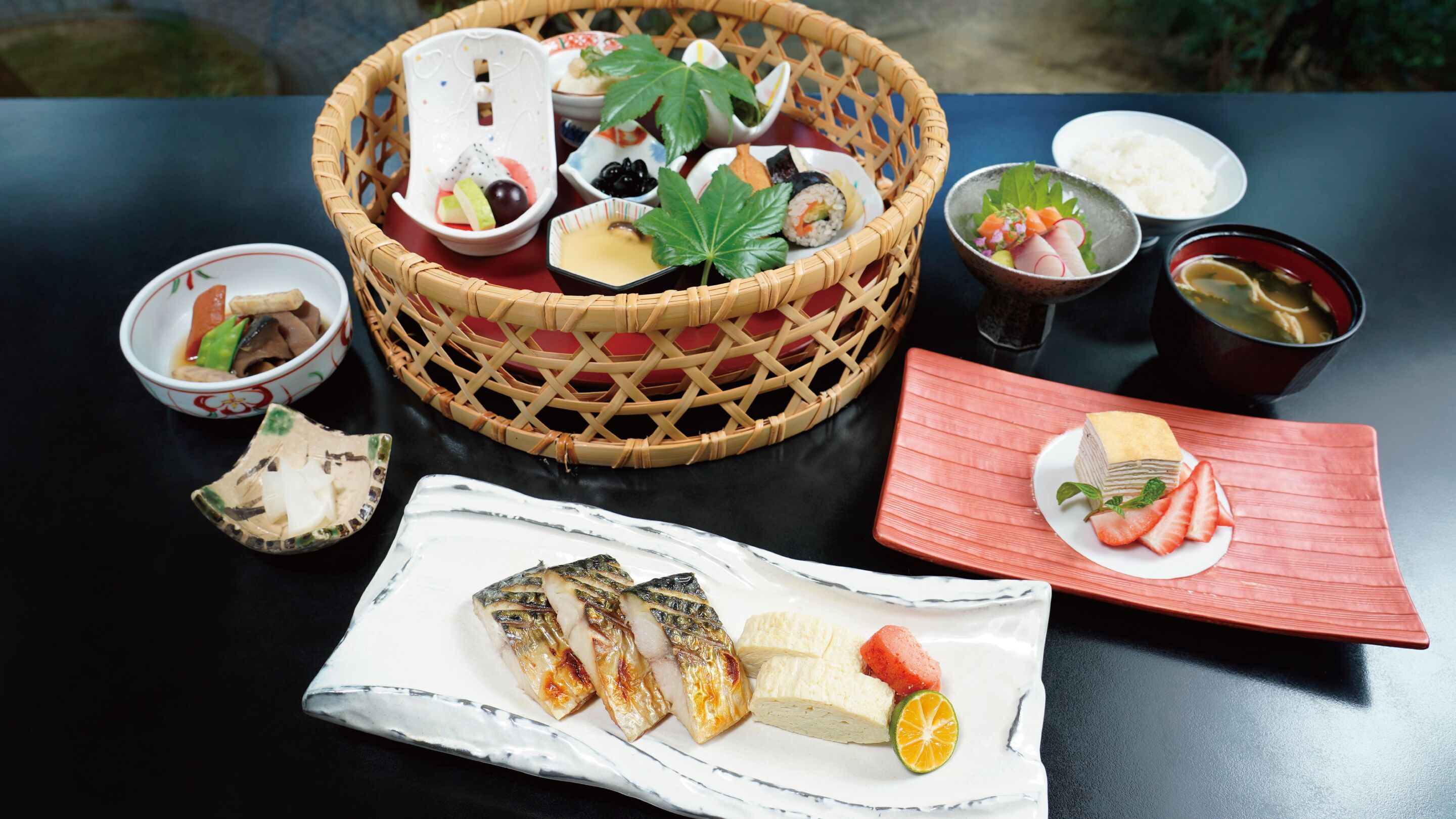 Una mesa servida con diversos platos, entre ellos sushi, un pescado y un postre con fresas.