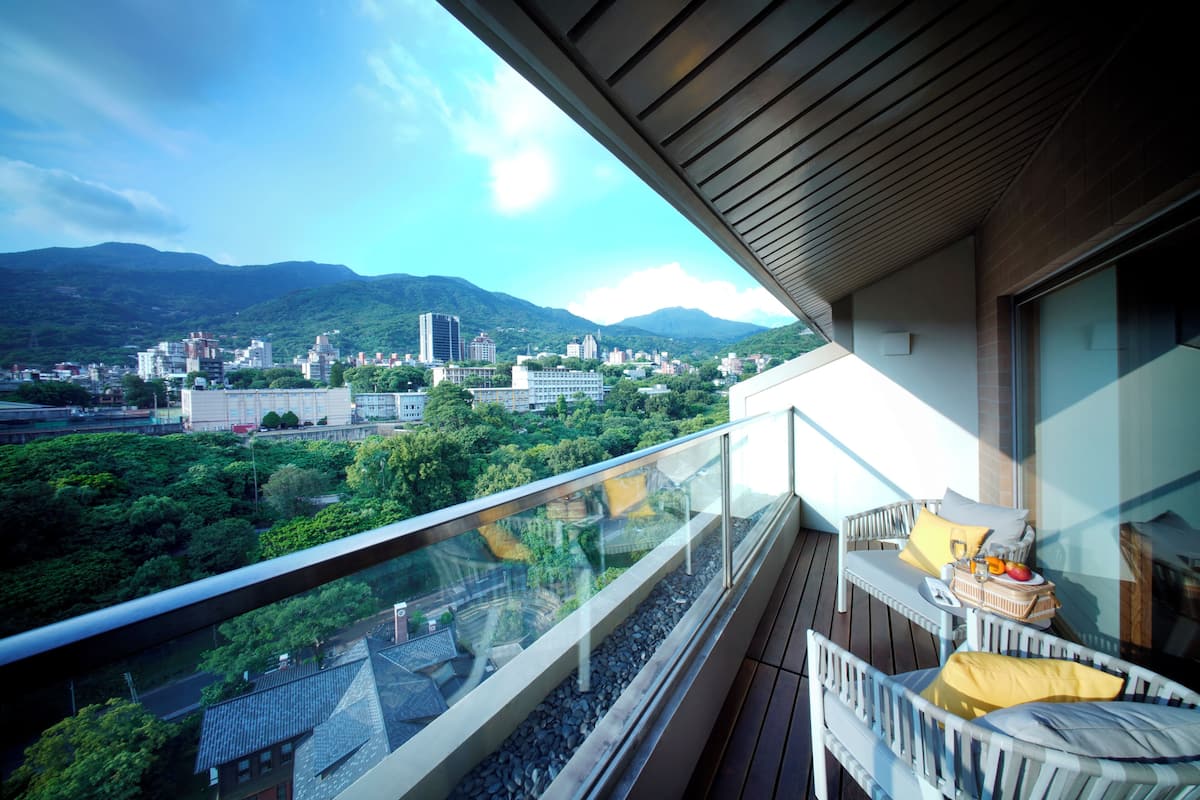 A balcony with a glass railing overlooking a cityscape with mountains in the background.