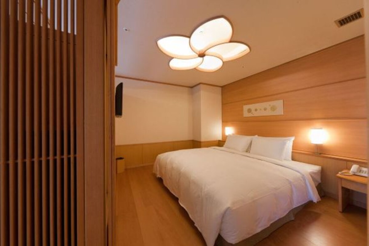 A hotel room with a bed, bedside lamps, a wooden headboard, and a ceiling fan.