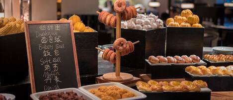 A bakery display with various baked goods and a sign listing items like doughnuts and muffins.
