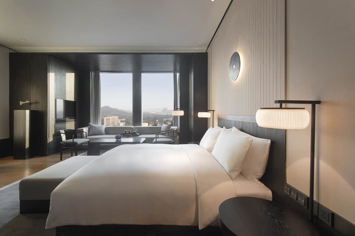 A modern hotel room with a large bed, a desk, and a view of the city.