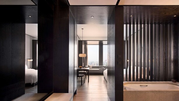 Una habitación de hotel moderna con piso de madera, un ventanal grande, un sofá, una mesa de comedor y una bañera.
