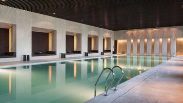 A modern indoor swimming pool with clear water, a sleek design, and a series of benches along the walls.
