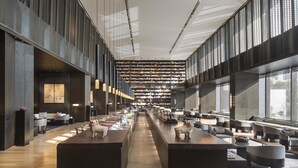 Un vestíbulo moderno de hotel con una barra central, rincones para sentarse y un amplio ventanal que proporciona luz natural.
