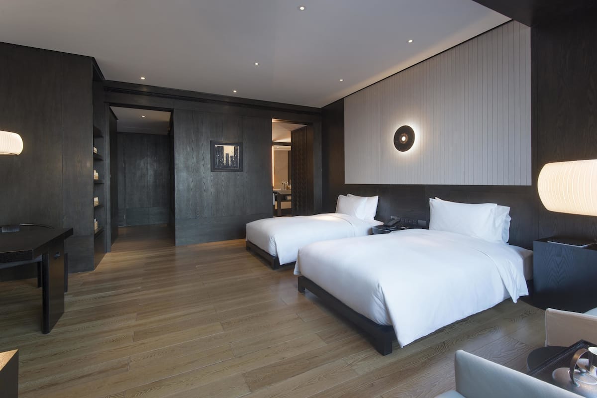 A modern hotel room with two beds, a desk, and a chair.