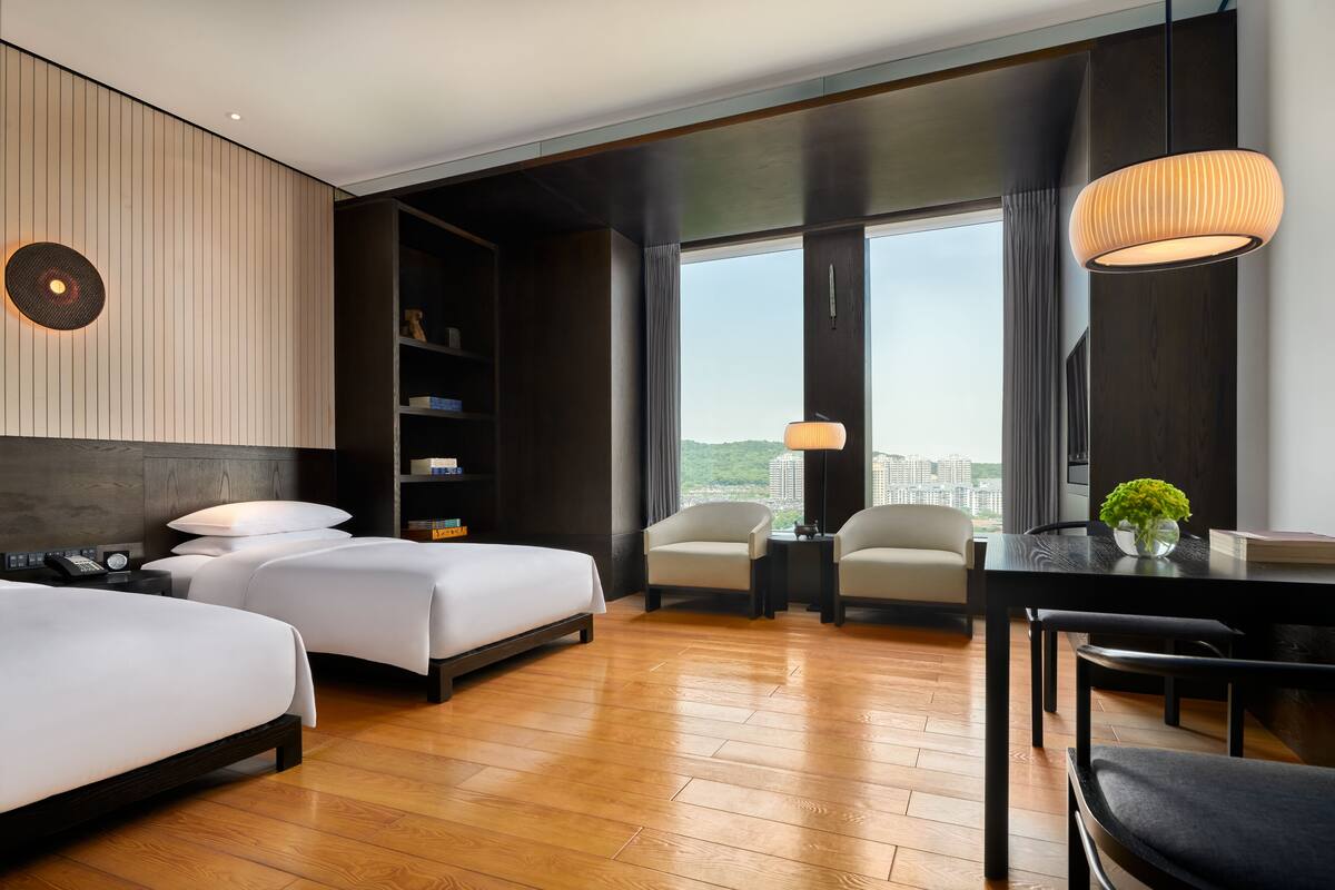A hotel room with two beds, a dining table, and a view of the city.
