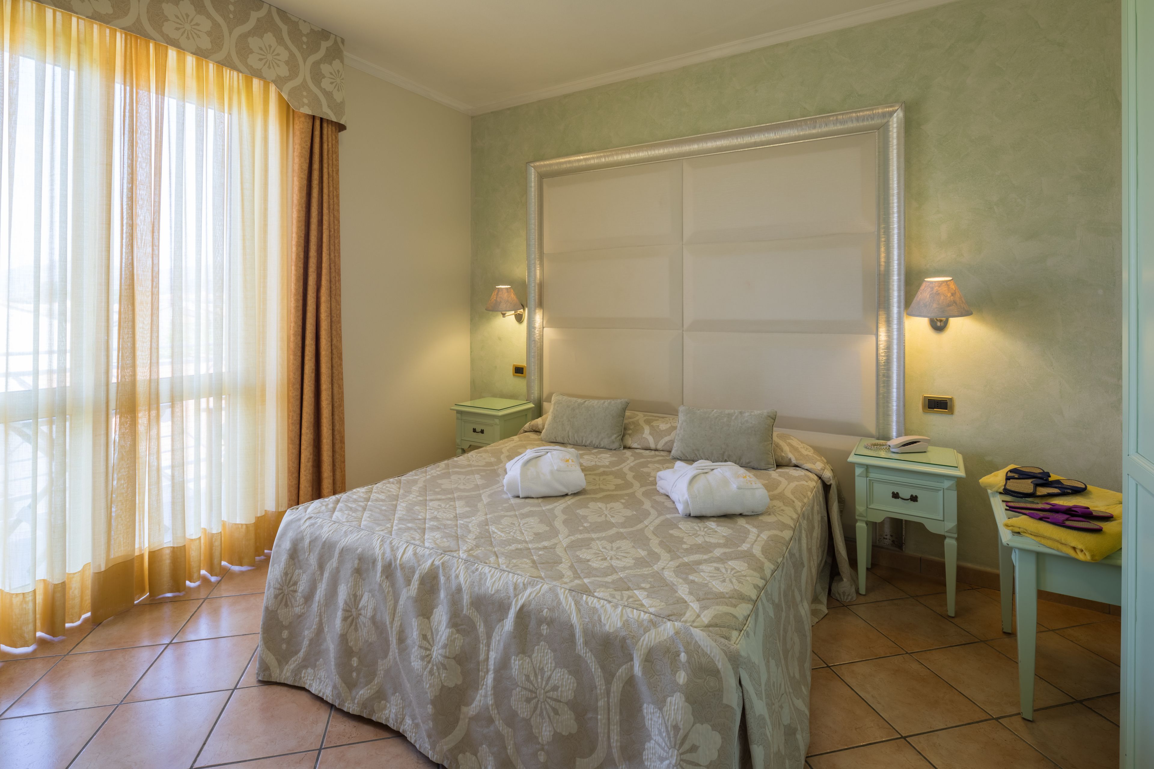 Un dormitorio ordenado con una cama grande, dos mesitas de noche y una ventana con cortinas.
