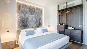 A modern bedroom with a large bed, a wall-mounted artwork, a wardrobe with hanging clothes, and a bedside table with a lamp. - Hotel Luna (Massa)