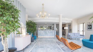 A modern hotel lobby with a marble floor, a reception desk, a chandelier, and seating areas. - Hotel Luna (Massa)