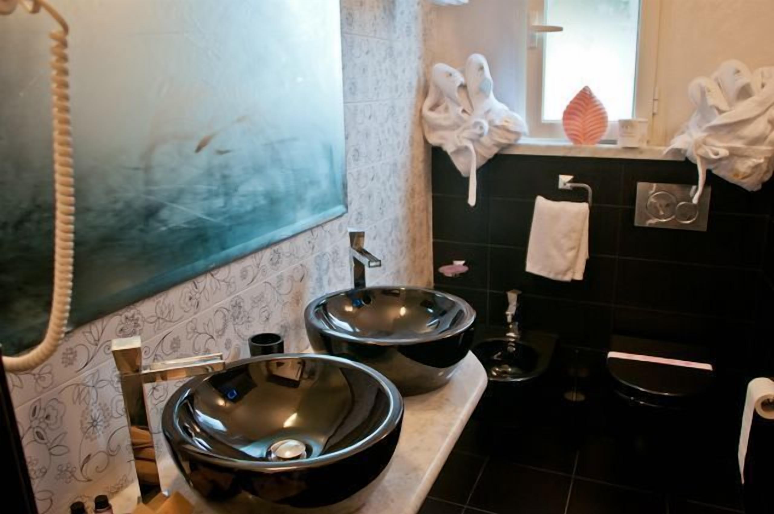 Casa de banho com duas pias grandes e modernas, um espelho e uma janela, com toalhas penduradas na parede.