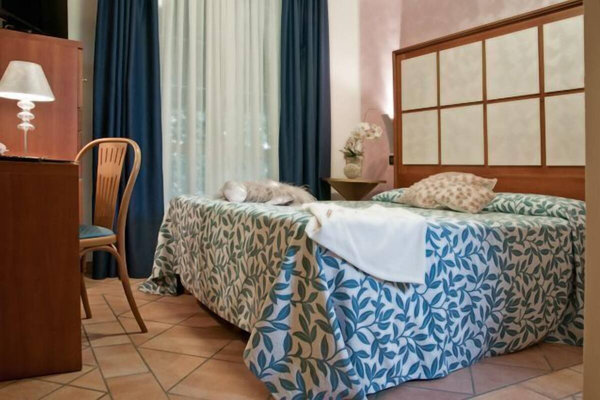 A bedroom with a bed, a chair, a desk, and a window with curtains.