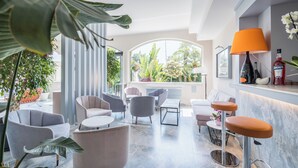 A modern lounge area with seating, a bar, and large windows offering a view of greenery. - Hotel Luna (Massa)