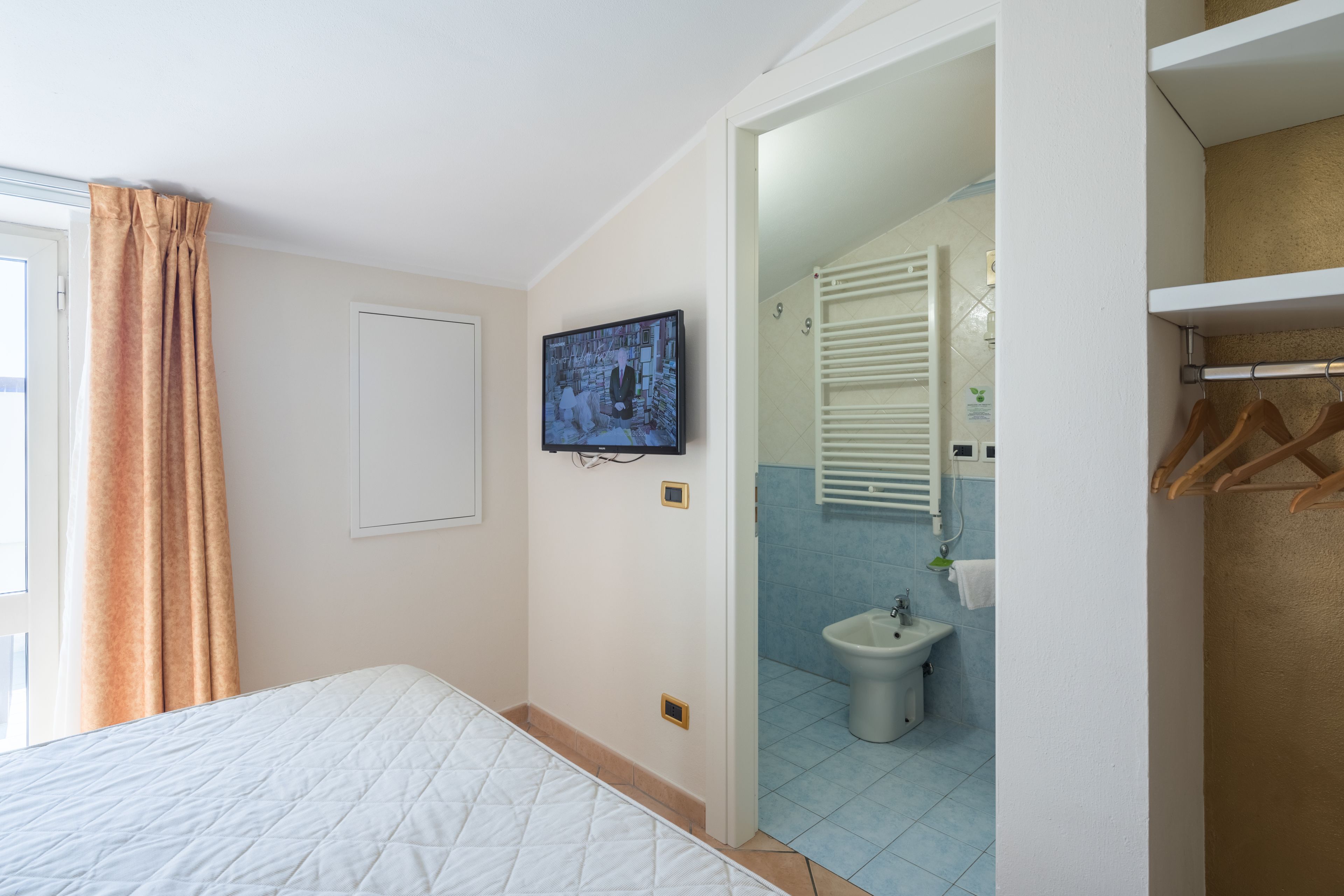 A bedroom with a bed, a television mounted on the wall, and a bathroom visible through an open door.