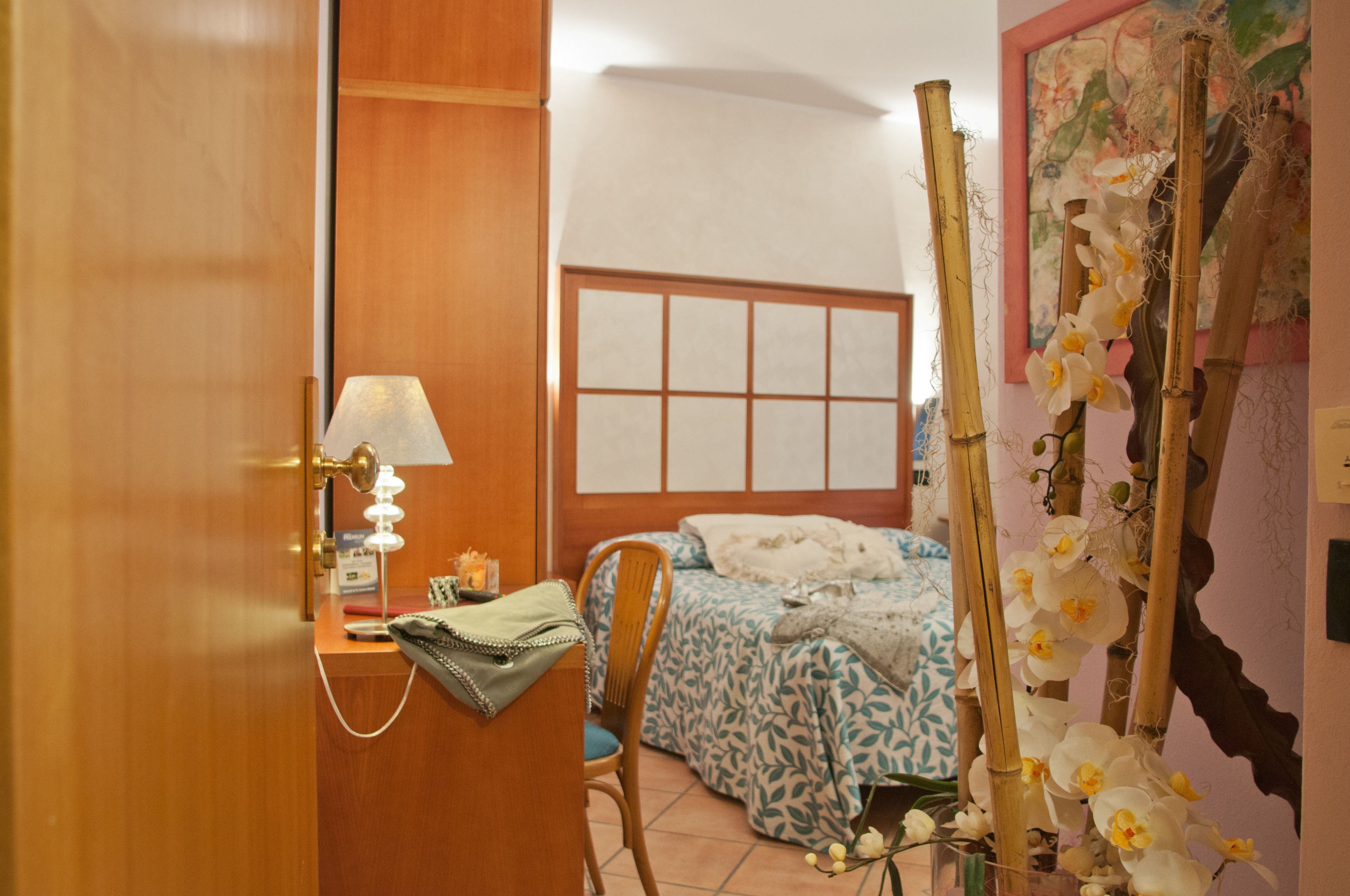 A bedroom with a bed, a desk with a lamp, a chair, and a decorative plant.