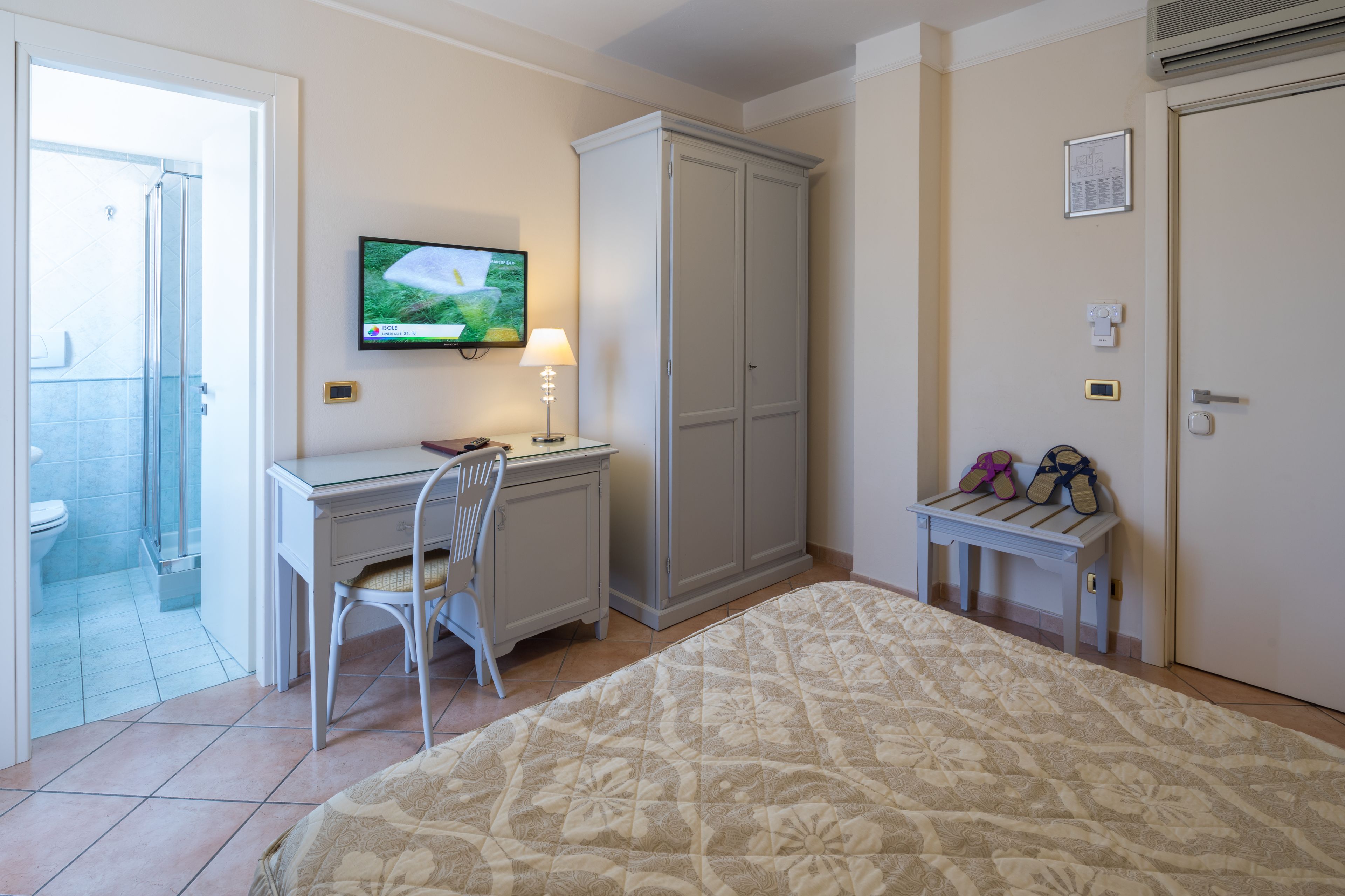 Een slaapkamer met een bed, een bureau, een stoel, een kledingkast, een televisie en een bijzettafeltje met schoenen.